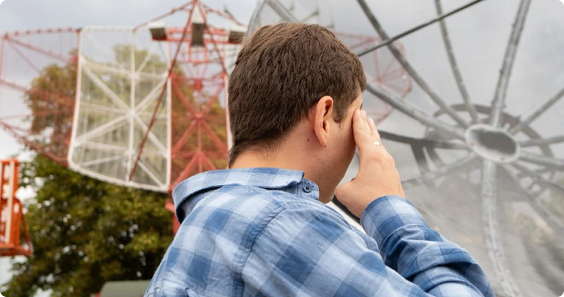 A man in a plaid shirt stands with his hand to his head, looking toward large outdoor radar dishes.