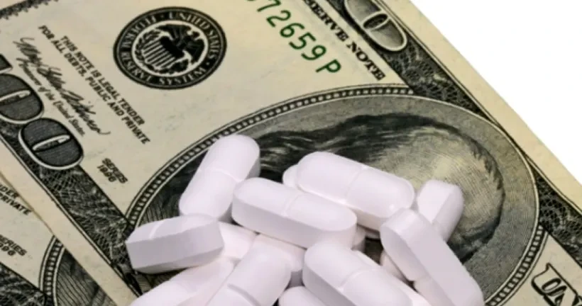 A small pile of white, oblong prescription medicine pills scattered on top of a one-hundred-dollar US bill.