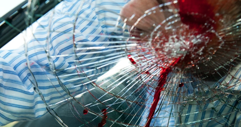 A severely shattered car windshield with a spiderweb fracture pattern and blood dripping down the glass.