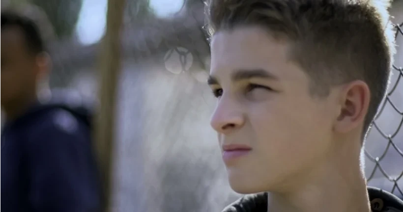 A young man looking thoughtfully into the distance with a chain-link fence.