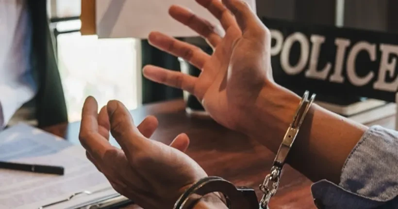 A person's handcuffed hands raised over a desk.