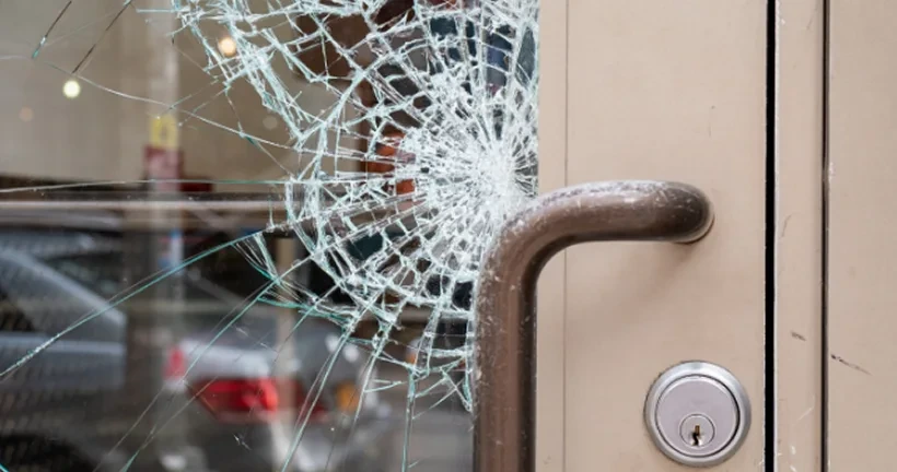 A glass door with a large shatter pattern right next to the metal handle.