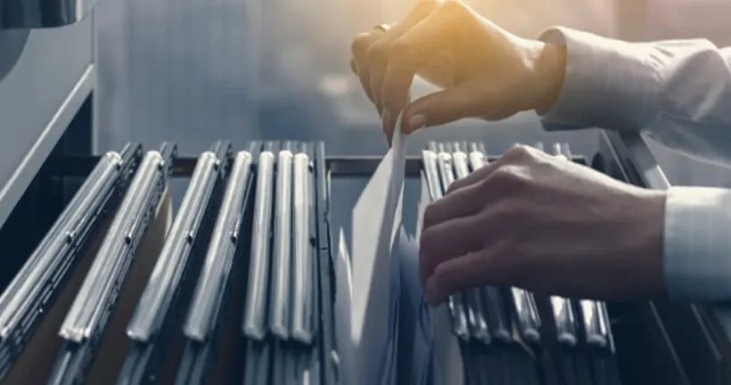A person's hands sorting through paper files in an open hanging folder organizer.